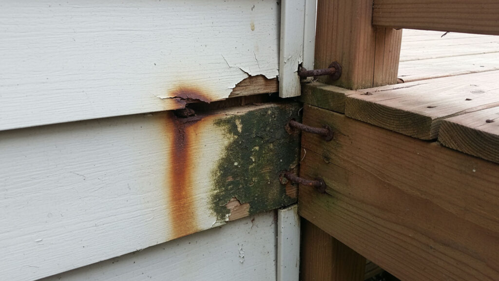Spokane deck ledger board pulling away from house siding with visible gap and rust stains